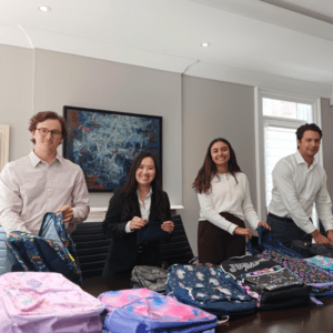 4 people in business attire smiling and packing colourful backpacks in an office boardroom.